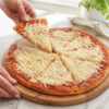 Pizza vegana cortada en tabla Pizza vegana con muzzarella vegetal cortada en tabla de madera, con manos levantando una porción